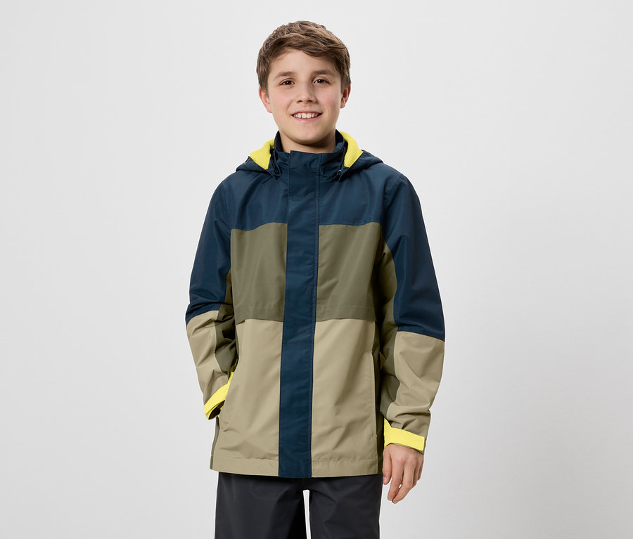 Ein lächelnder Junge steht vor einem weißen Hintergrund und trägt eine farblich abgesetzte Jacke mit gelbem Futter.
