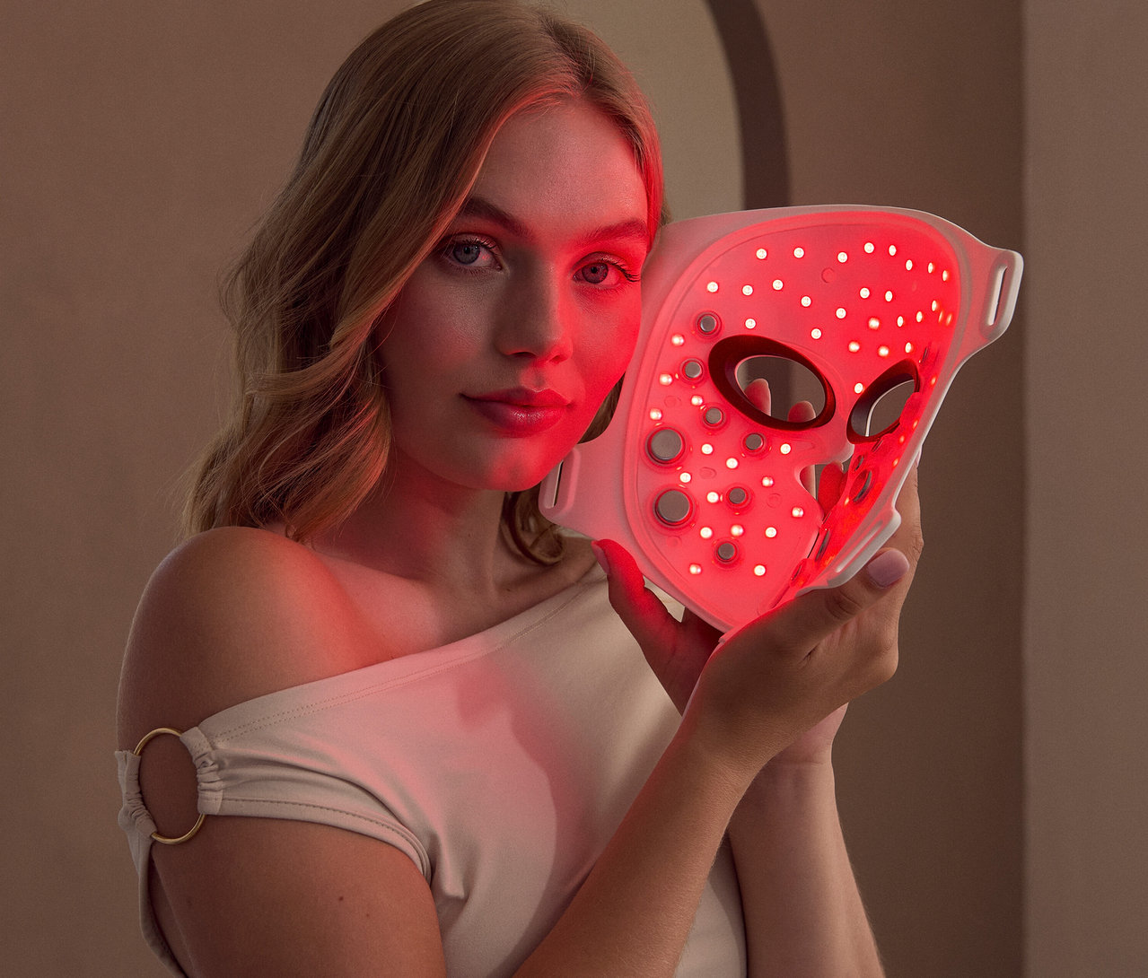 Frau hält eine Silk'n LED Gesichtsmaske mit EMS in der Hand, die rot leuchtet.