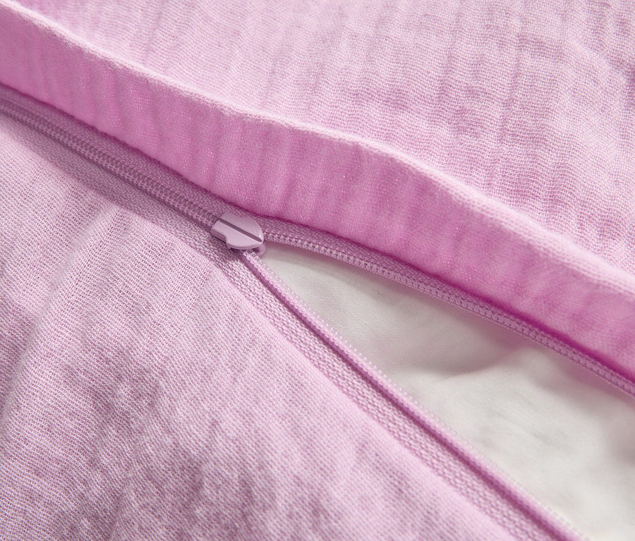 Nahaufnahme eines teilweise geöffneten, lavendelfarbenen Bettbezugs mit Reißverschluss, der einen Blick auf ein weißes Kissen darunter freigibt.