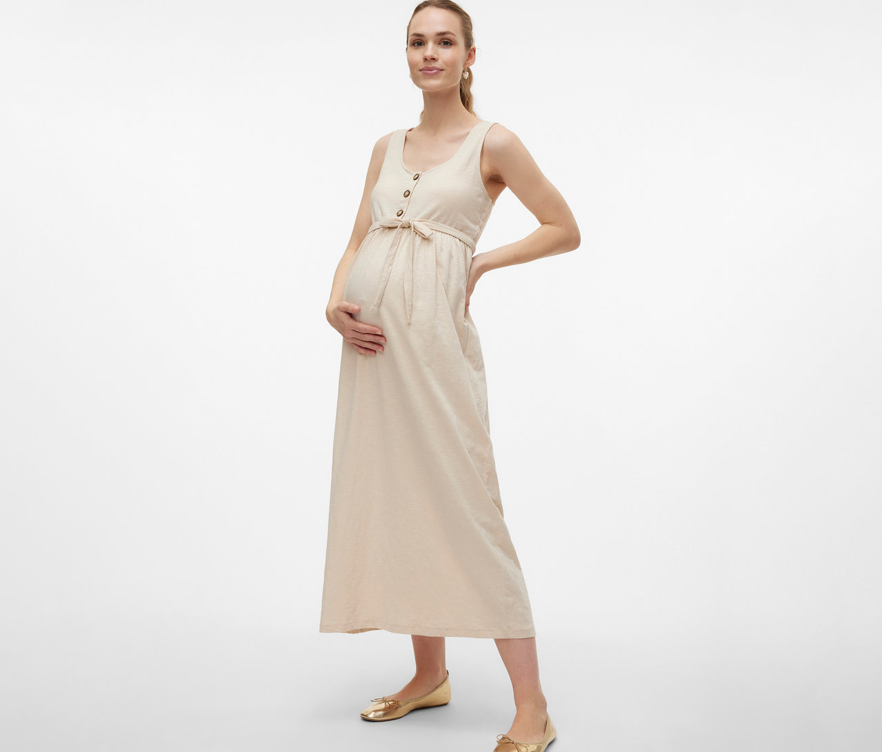 Schwangere Frau im MAMALICIOUS Schwangerschaftskleid »MLEVI LIA«, mit Gürtel und Knöpfen, posiert mit Händen an Bauch und Hüfte.