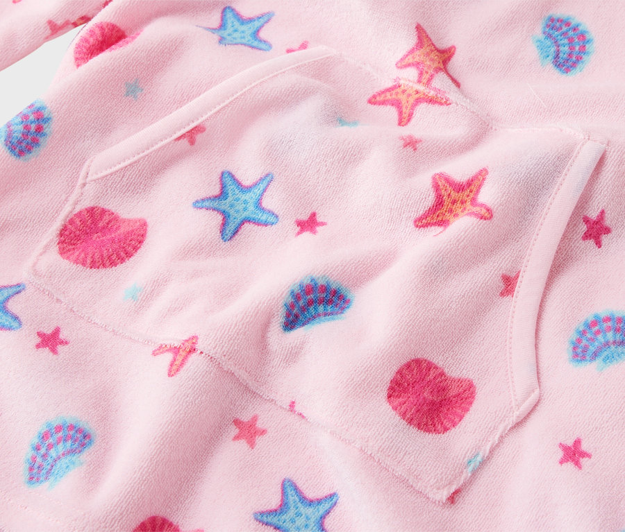 Nahaufnahme eines rosa Kinderbademantels mit Seestern- und Muschelmuster und einer aufgesetzten Tasche.