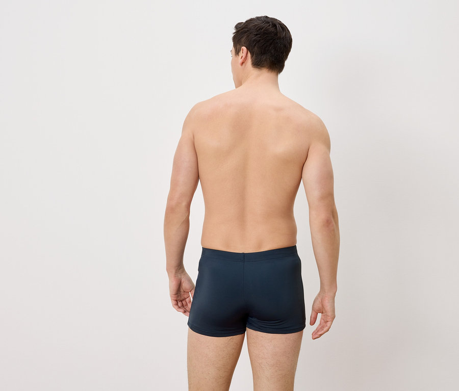 Ein Mann von hinten, der blaue Badehosen trägt.
