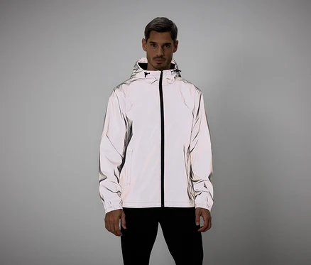 Mann mit grauen Haaren trägt eine reflektierende Jacke mit Kapuze und schwarzem Reißverschluss vor grauem Hintergrund.