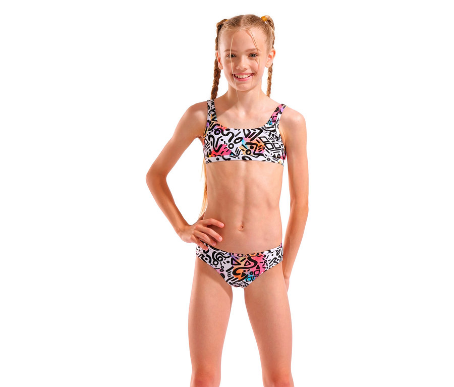 Mädchen mit blonden Zöpfen, das einen weißen Bikini mit geometrischen Mustern trägt und mit einer Hand in der Hüfte posiert.