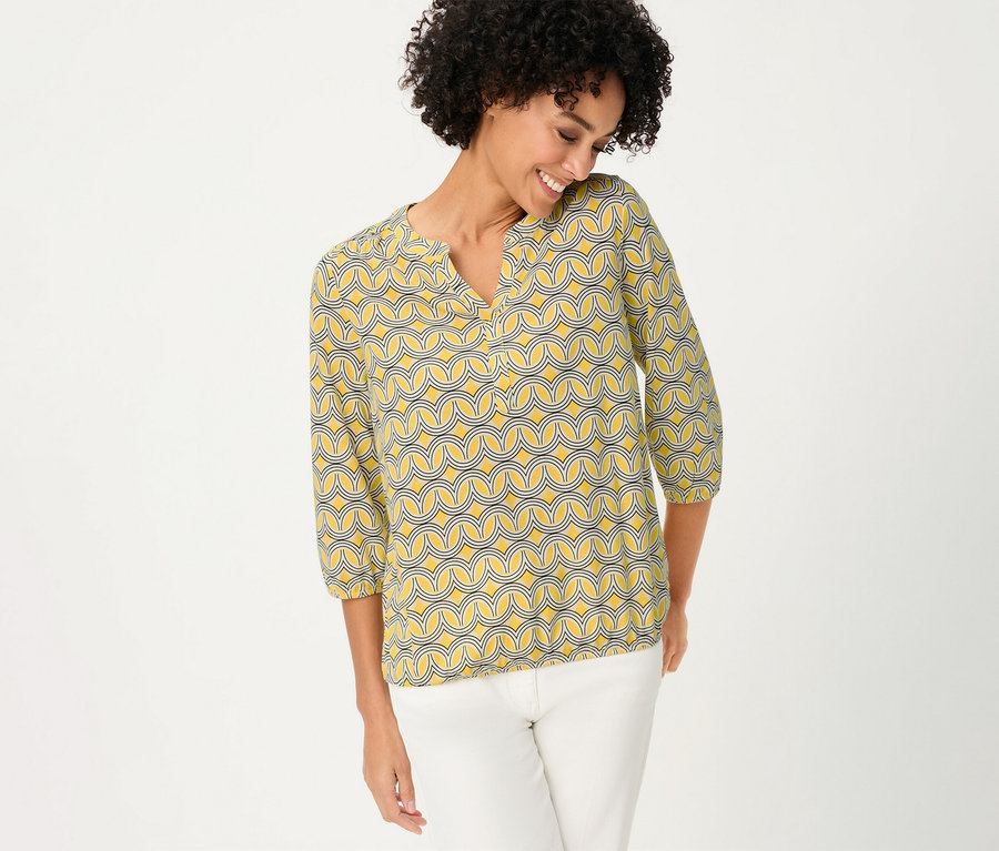 Frau trägt ein Olsen 3/4-Blusenshirt mit gelbem Muster und weiße Hose.