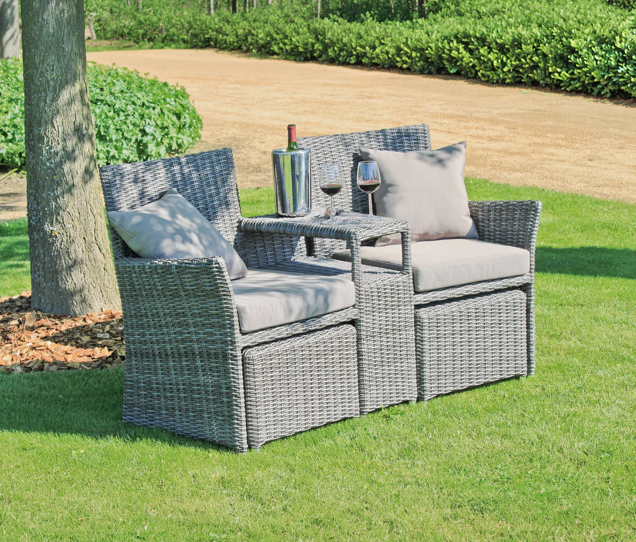 Graue Korbsessel mit Tisch stehen auf einer Wiese. Auf dem Tisch stehen ein Weinkühler, eine Flasche Wein und zwei Weingläser.