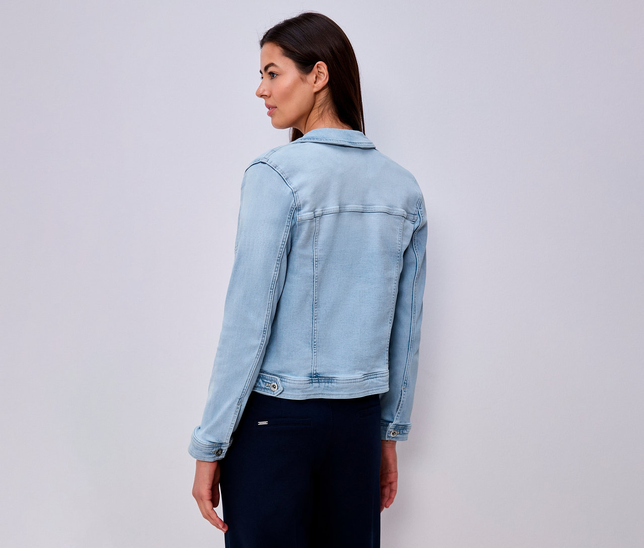 Frau von hinten, trägt hellblaue Jeansjacke und langen, dunkelblauen Rock.