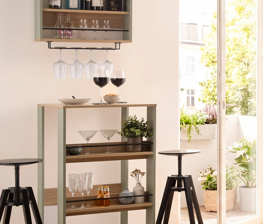 Bar mit Spirituosen und Gläsern, darüber ein Hängeregal. Zwei Barhocker stehen davor.