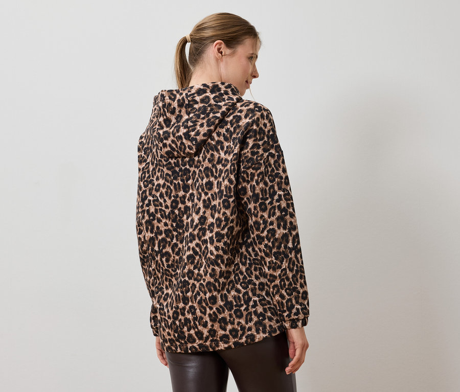 Rückansicht einer Frau mit Pferdeschwanz, die eine Kapuzenjacke mit Leopardenmuster und braune Lederhose trägt.