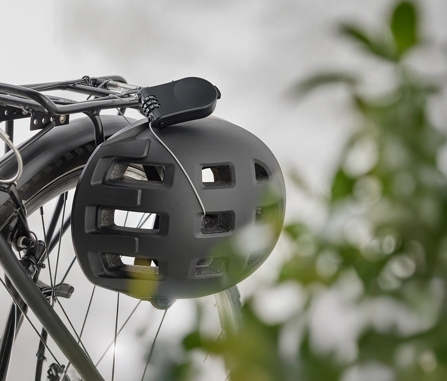 Ein schwarzer Fahrradhelm hängt mit einem Zahlenschloss an einem Fahrradgepäckträger.