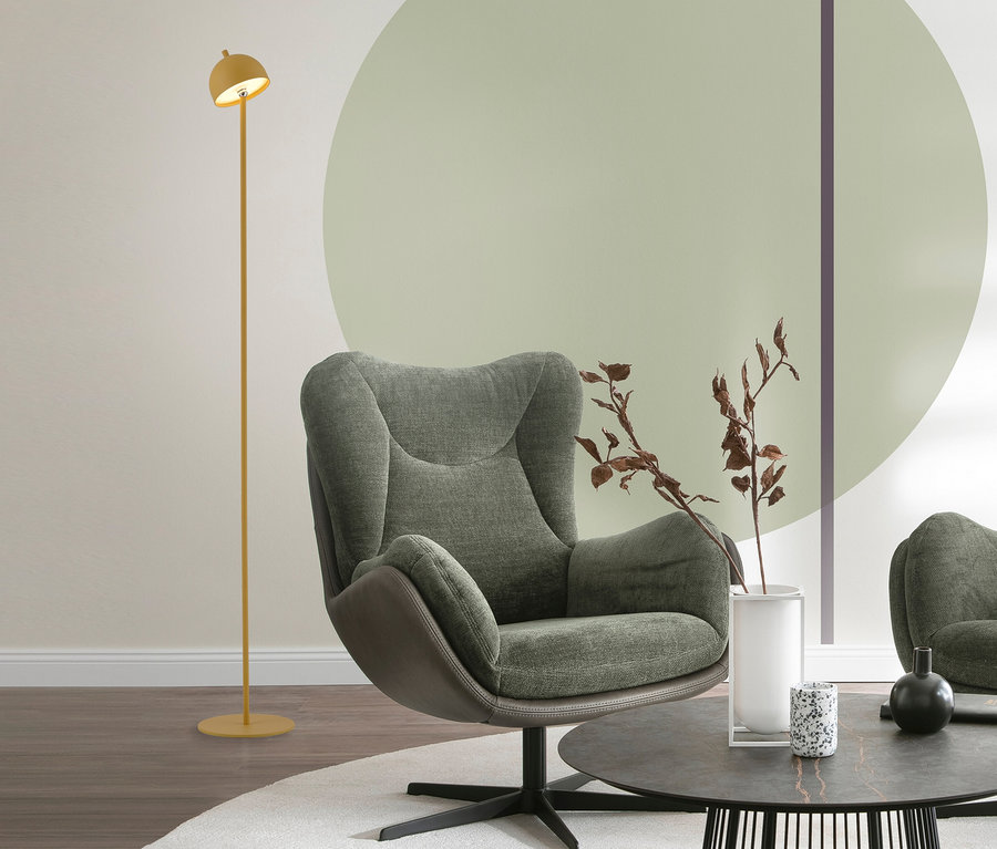Ein Wohnzimmer mit einem grünen Sessel, einem runden Couchtisch mit Deko und einer gelben SCHÖNER WOHNEN-Kollektion Akku-Stehleuchte »Bellis«. Die Leuchte steht links neben dem Sessel.