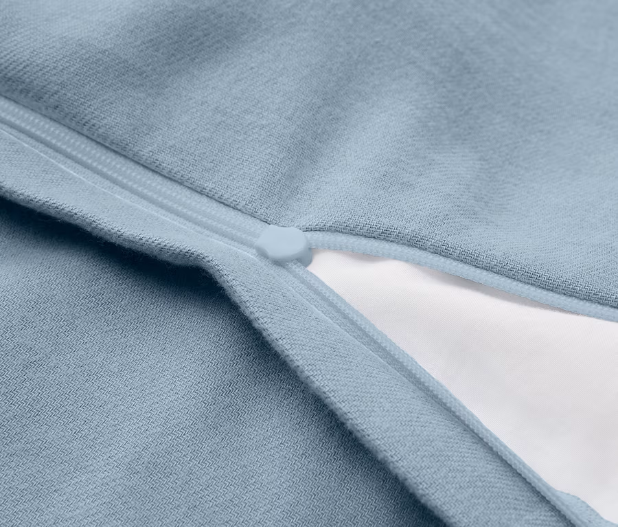 Nahaufnahme eines hellblauen Stoffes mit einem teilweise geöffneten Reißverschluss, der weißen Stoff darunter zeigt.