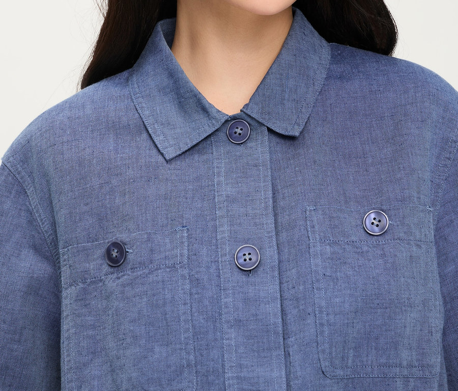 Nahaufnahme einer Person, die eine blaue Olsen Jeansjacke mit Kragen, Knöpfen und aufgesetzten Brusttaschen trägt.
