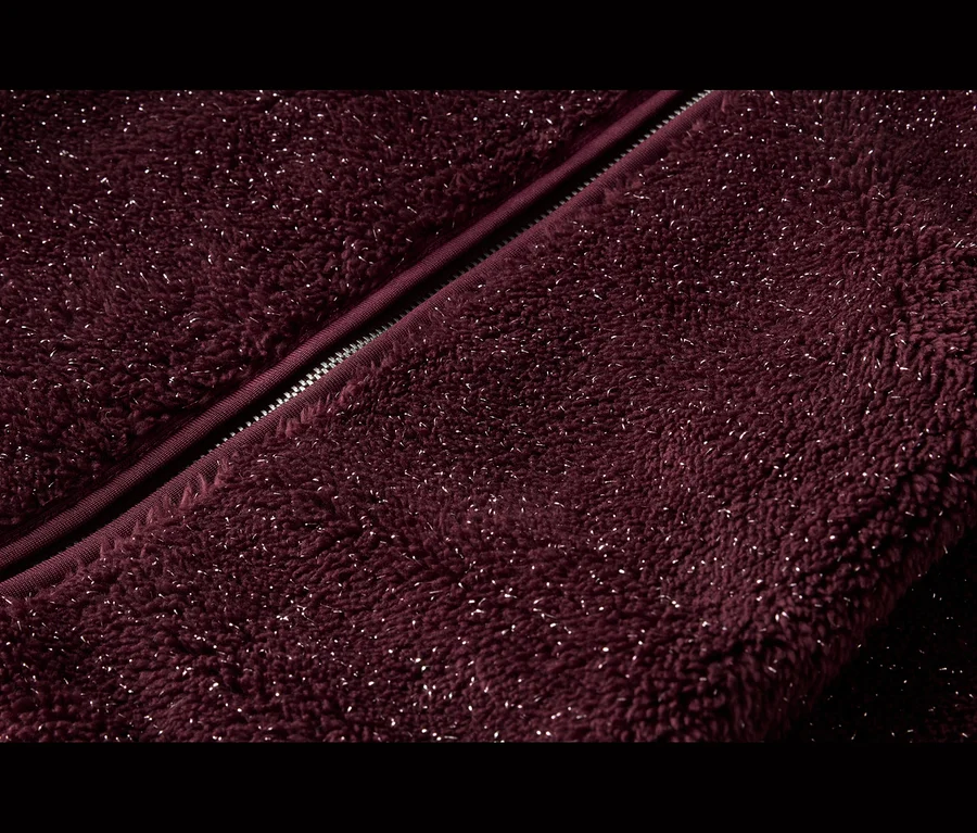 Nahaufnahme eines burgunderroten Fleece-Stoffs mit silbernen Glitzerfäden und einem diagonal verlaufenden Reißverschluss.