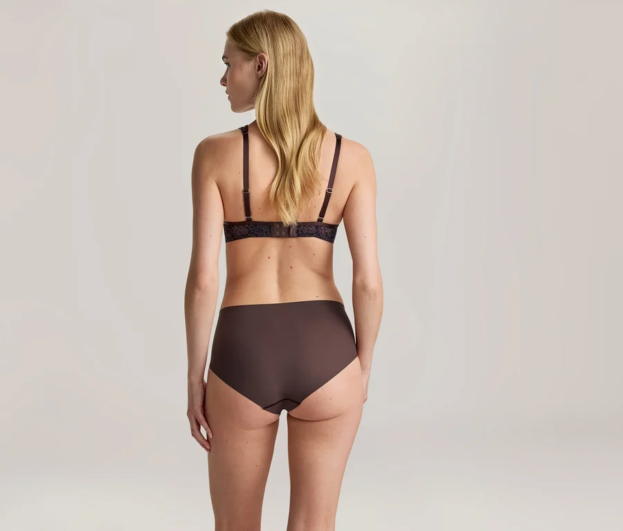 Eine Frau von hinten, die einen dunkelbraunen BH mit Spitzendetails und eine schlichte, dunkelbraune High-Waist-Hose trägt. Ihr blondes Haar ist offen.