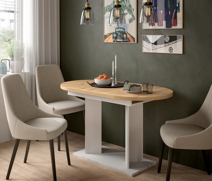 Ein ovaler Esstisch mit heller Holzplatte und weißem Fuß, umgeben von drei beigen Polsterstühlen. Auf dem Tisch stehen Orangen, Kerzen, Teller und Gläser. Drei Pendelleuchten hängen darüber, und gerahmte Bilder schmücken die dunkle Wand.