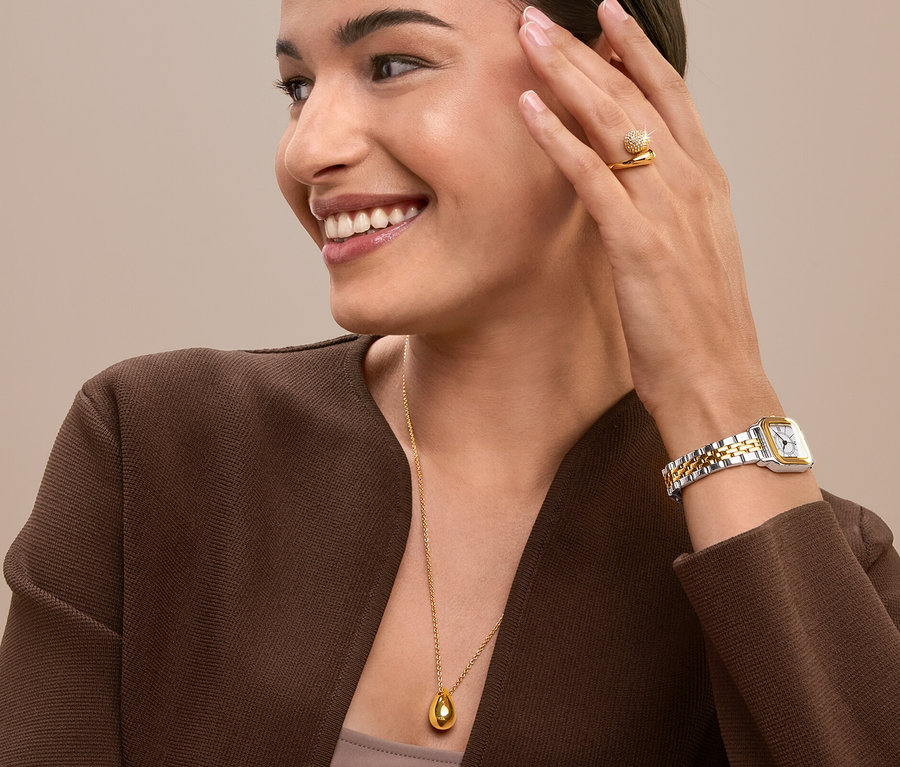 Lächelnde Frau berührt ihr Gesicht und trägt einen goldenen Ring, eine Uhr und eine Halskette.