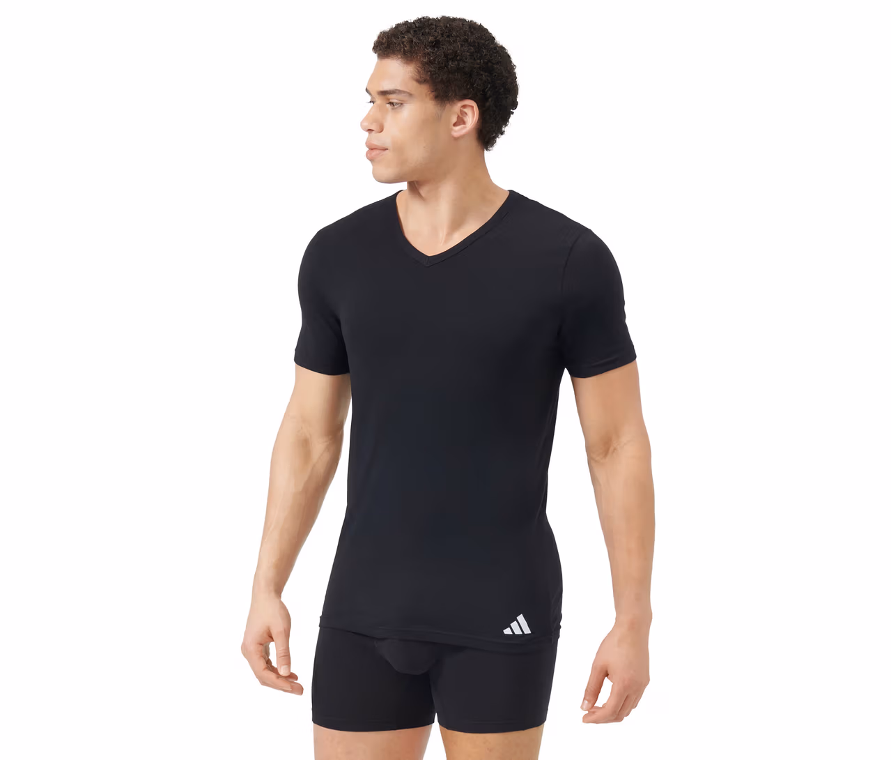 Mann trägt schwarzes V-Ausschnitt T-Shirt und schwarze Boxershorts. Das T-Shirt hat ein weißes Logo unten links. Der Mann blickt nach rechts.