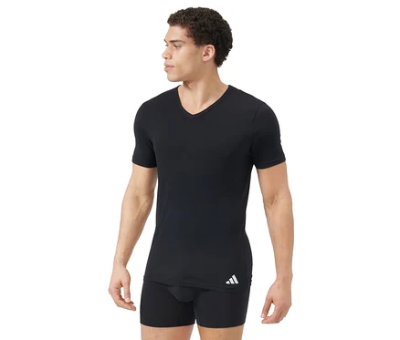 Mann trägt schwarzes V-Ausschnitt T-Shirt und schwarze Boxershorts. Das T-Shirt hat ein weißes Logo unten links. Der Mann blickt nach rechts.