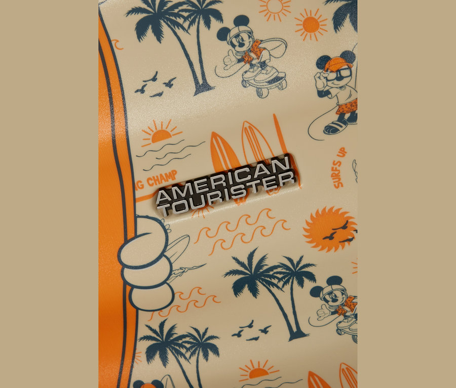 Nahaufnahme einer cremefarbenen Oberfläche, wahrscheinlich Gepäck, mit einem Strandmuster. Das Muster zeigt dunkelblaue Palmen, orangefarbene Sonnen, Wellen, Surfbretter und Vögel. Micky Maus ist in dunkelblauer Umrandung mit orangefarbenen Akzenten dargestellt, wie er Skateboard fährt und surft. Ein silbernes 'AMERICAN TOURISTER'-Logo mit schwarzem Text ist mittig platziert.