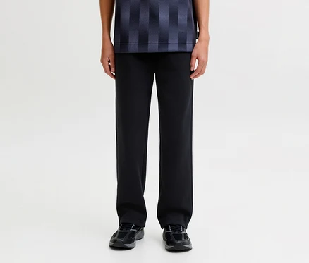 Eine Person steht und trägt eine schwarze Jack&Jones Bradley Sweatpants, ein dunkelblau gemustertes Shirt und dunkle Sneaker.