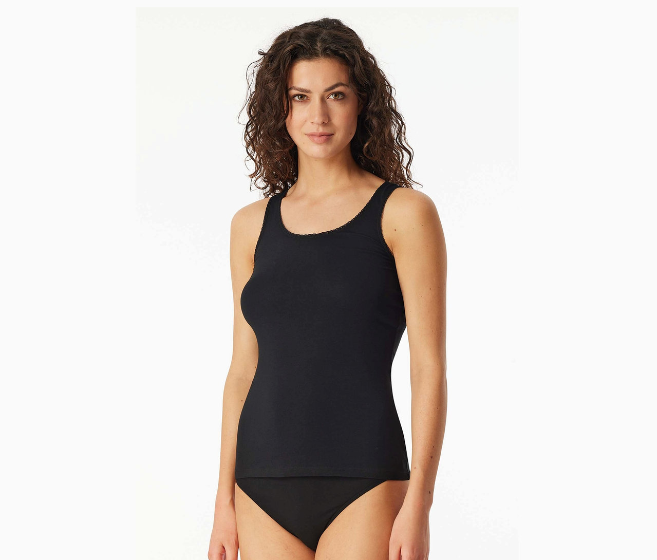 Frau mit gewelltem Haar trägt ein schwarzes Tanktop und einen schwarzen Slip.