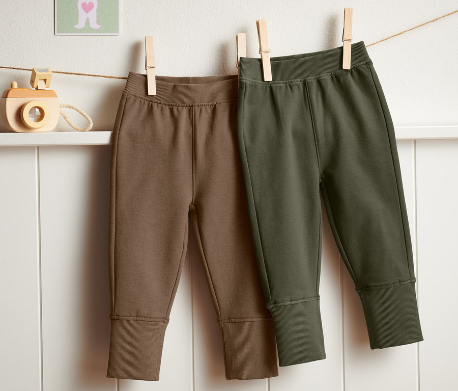 Zwei Jogginghosen (2 Stück) in Braun und Olivgrün hängen an einer Wäscheleine.