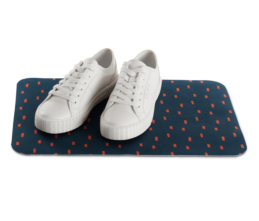 Zwei weiße Turnschuhe auf einer blauen Napfunterlage aus Vlies mit orangefarbenen Quadraten.