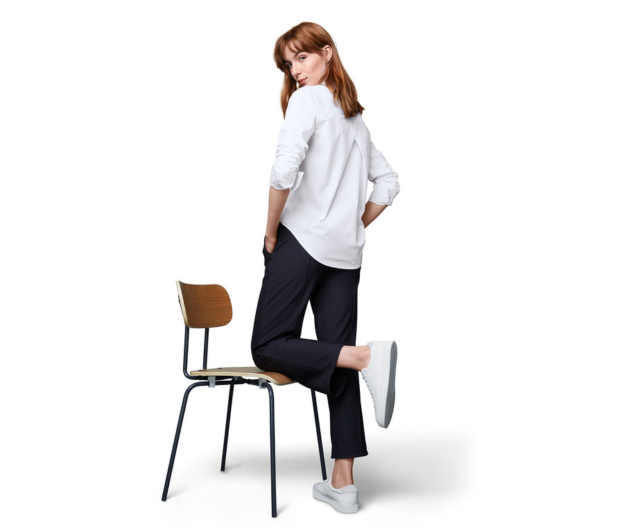 Frau posiert auf einem Stuhl und trägt eine Funktionsbluse.