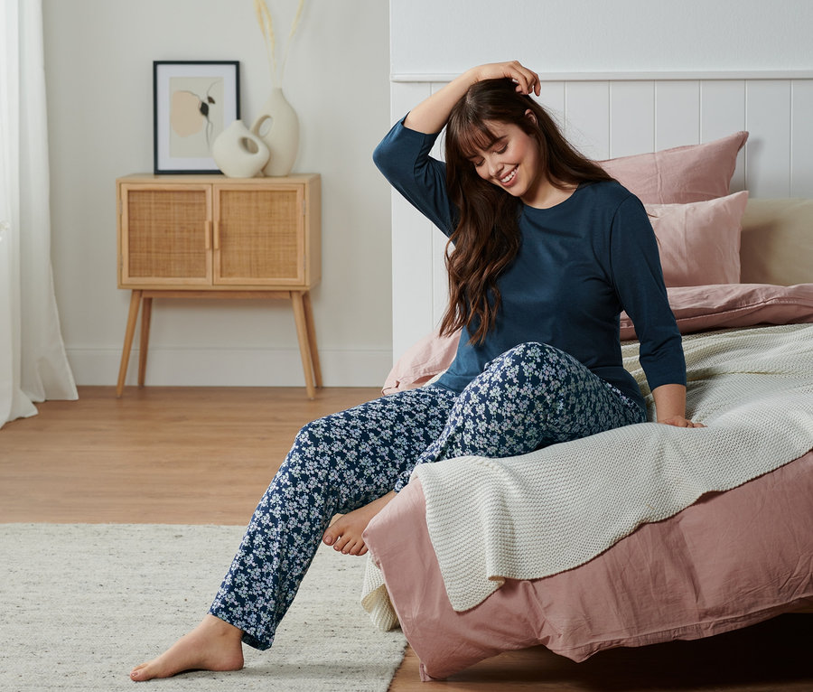 Frau sitzt im Pyjama auf dem Bett.