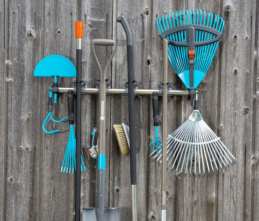 Verschiedene Gartengeräte, darunter Rechen und eine Schaufel, hängen an einem Gerätehalter an einer Holzwand. GARDENA »Gerätehalter« ist auch sichtbar.