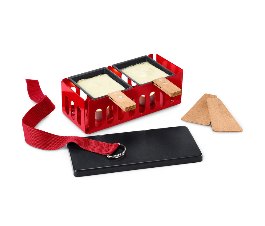 Raclette für 2 mit rotem Rahmen, zwei Pfannen mit geschmolzenem Käse, einer schwarzen Platte und Holzspateln.