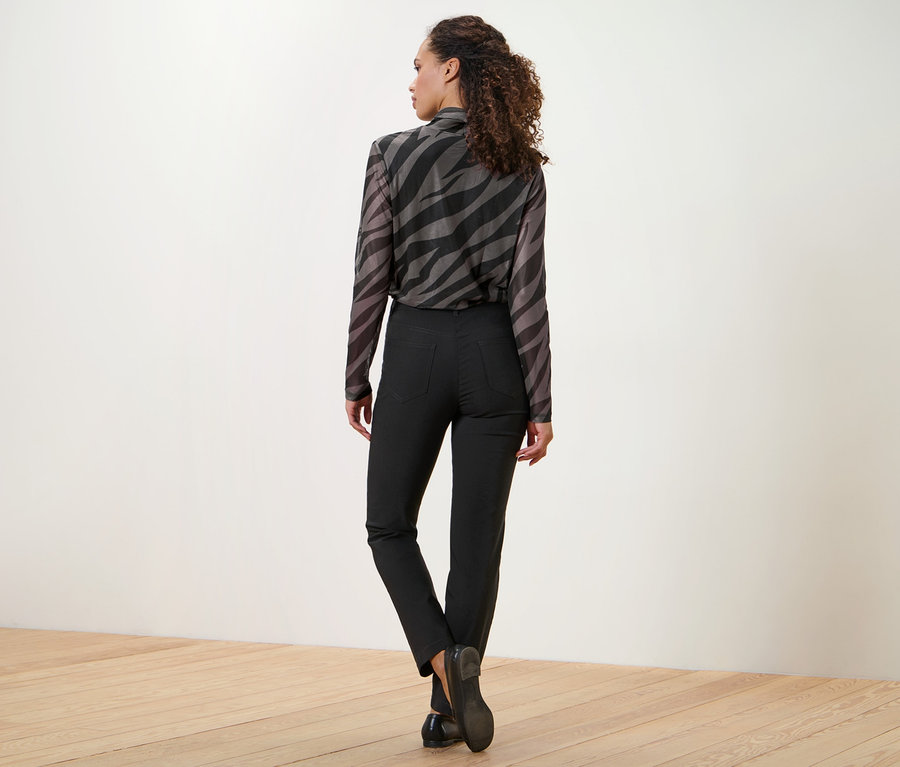 Frau blickt über die Schulter, trägt eine Bluse mit Animal-Print und eine schwarze Bengalin-Hose.