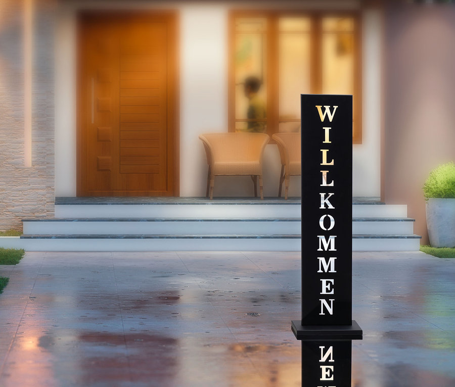 Schwarzes Standschild »Willkommen« steht vor einem Haus.