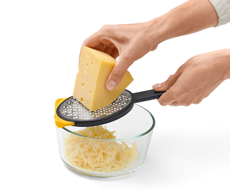Person reibt Käse mit einer 2-seitigen Schnellreibe in eine Glasschüssel.