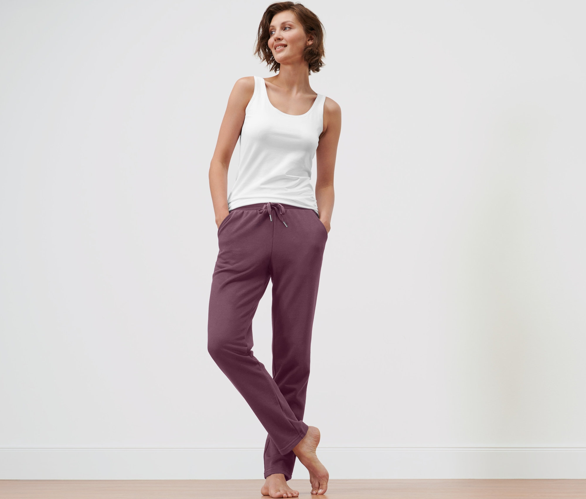 Frau steht mit Händen in den Taschen einer auberginefarbenen Loungewear-Hose.