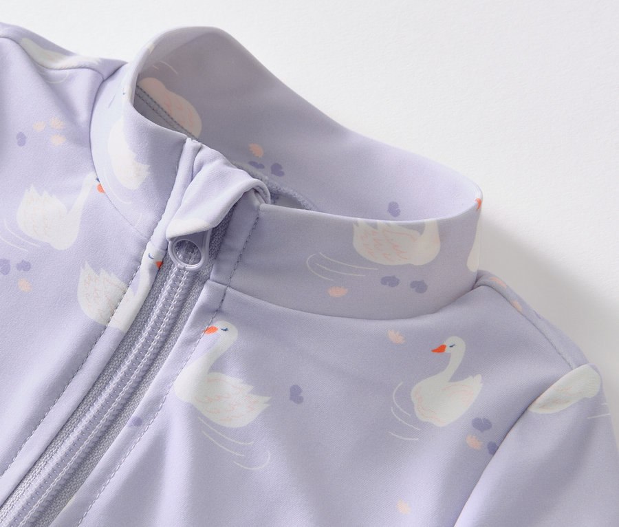 Detailansicht eines lila Baby-Einteilers mit Schwanenmuster und Reißverschluss, UV-Schutzfaktor 80.