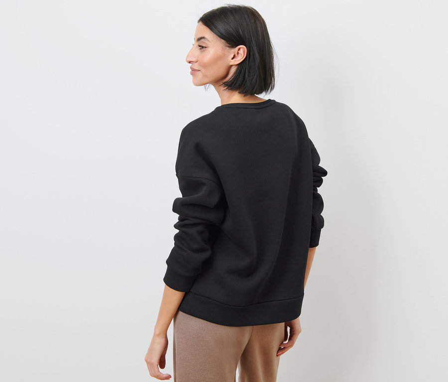 Frau blickt über die Schulter und trägt ein schwarzes Sweatshirt.