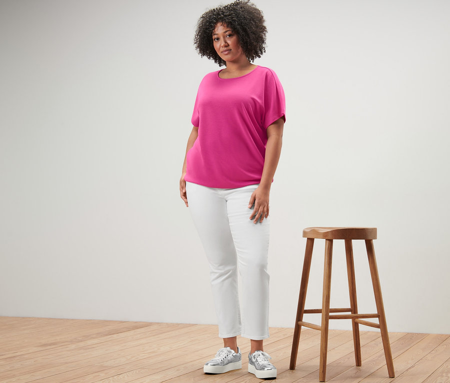 Frau steht neben einem Holzhocker und trägt ein Blusenshirt und eine Colored Jeans – Fit »Emma«, creme.