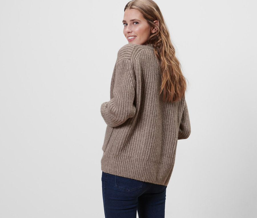 Frau blickt über die Schulter und trägt einen grob gestrickten Cardigan mit Wolle und Jeans.