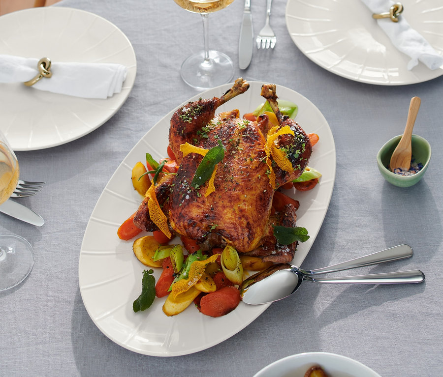 Gebratenes Huhn auf einer Servierplatte mit Beilagen auf einem Tisch.