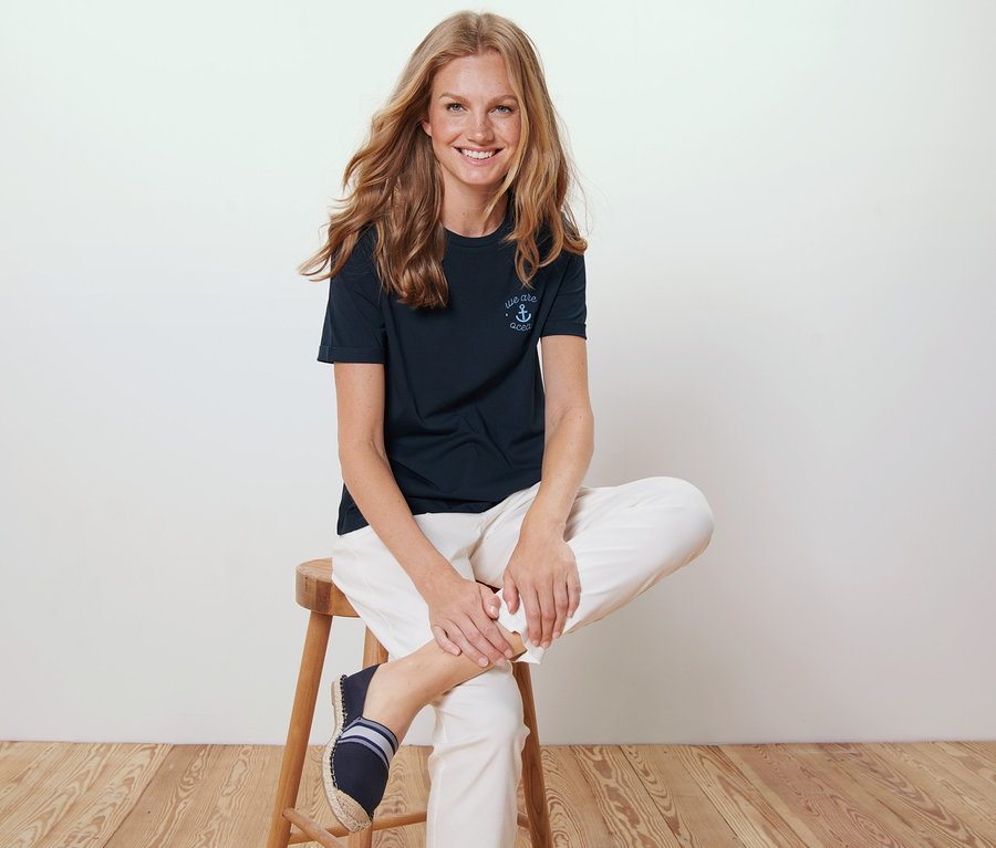 Frau sitzt auf einem Hocker und trägt ein dunkelblaues T-Shirt mit Stickerei.