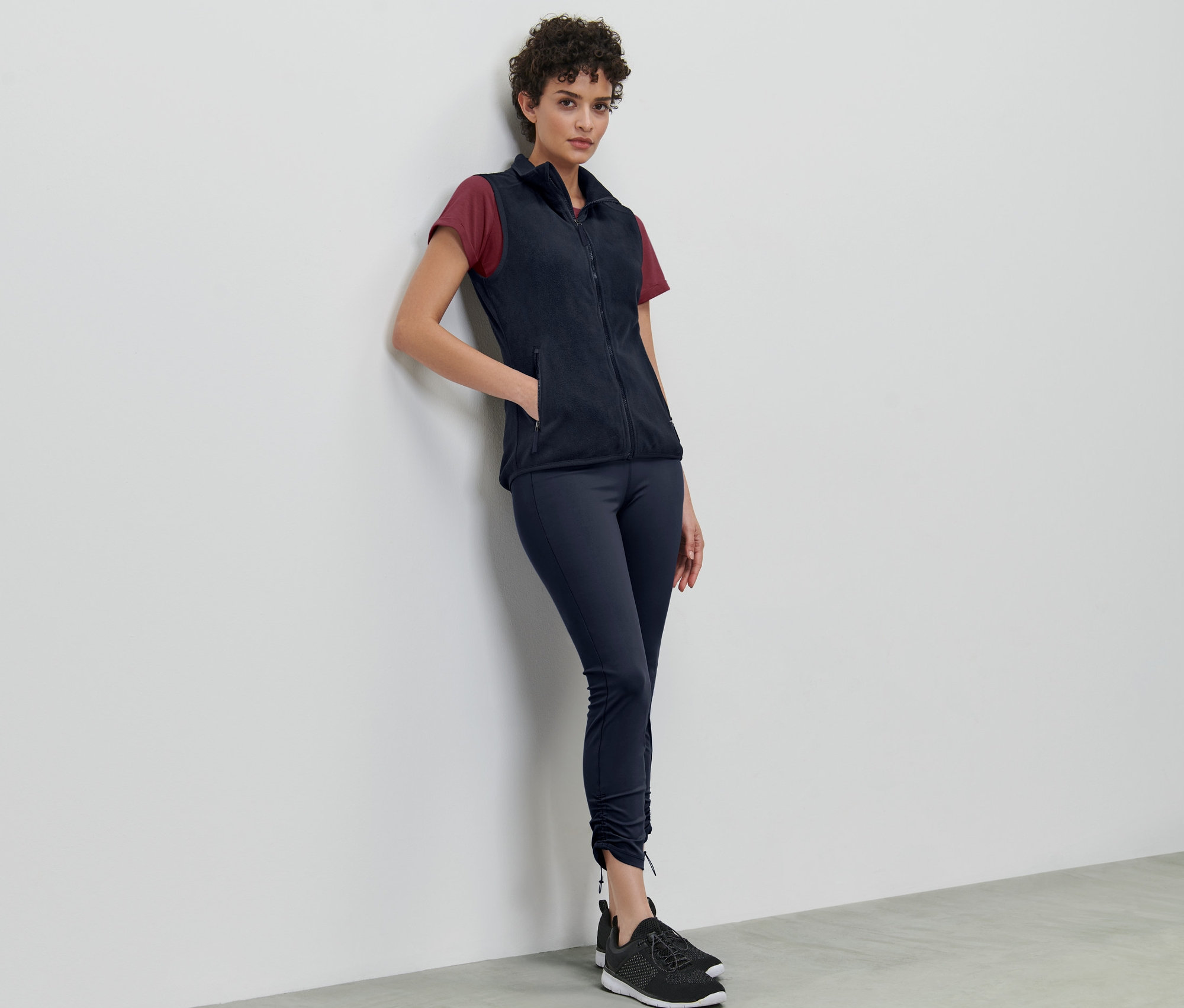 Frau lehnt an Wand und trägt eine Fleece-Weste.