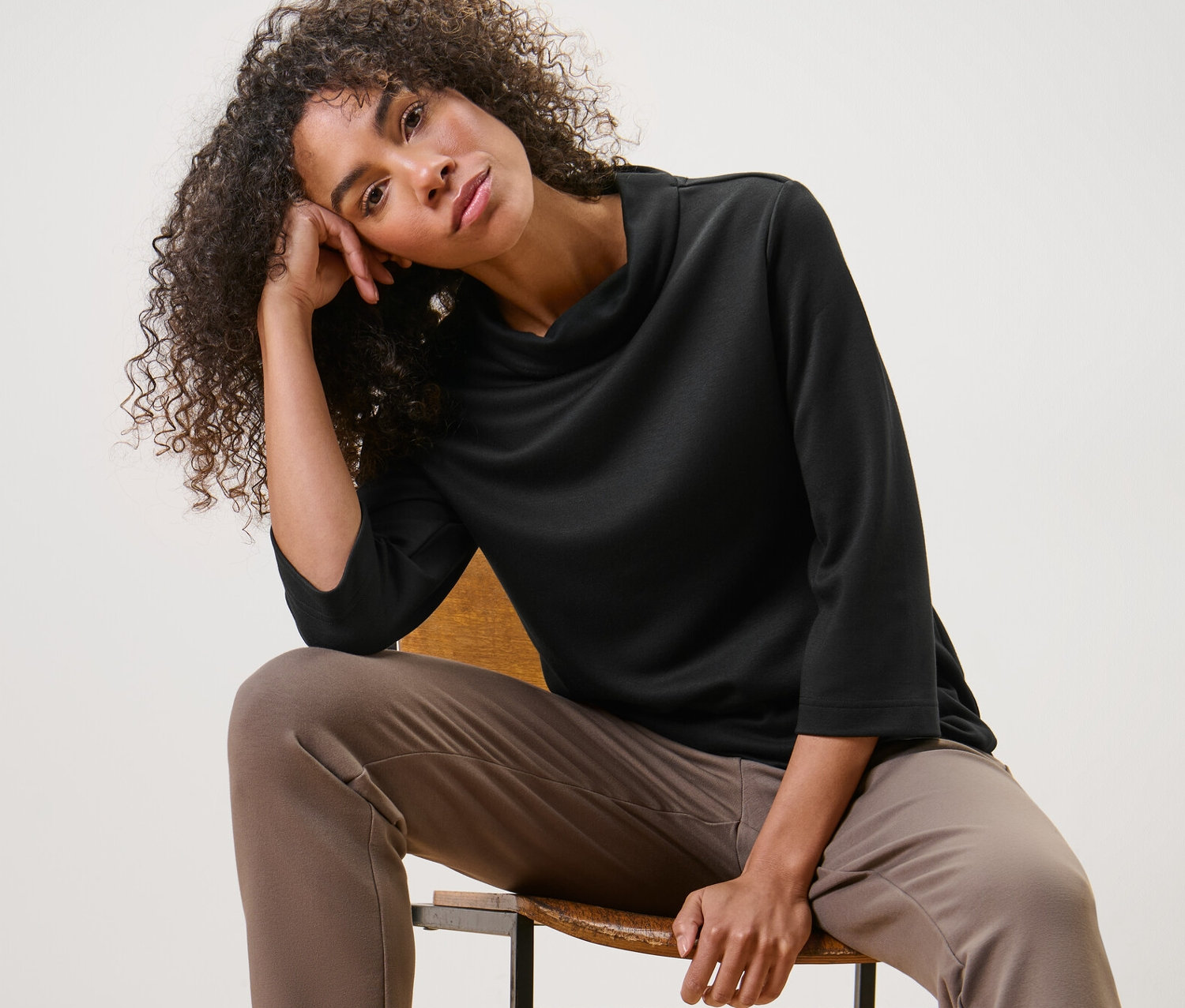 Porträt einer Frau, die in einem schwarzen Sweatshirt mit 3/4-Arm auf einem Stuhl sitzt.