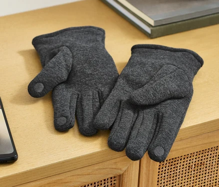 Zwei Sweathandschuhe liegen auf einer Holzkommode neben einem Handy.