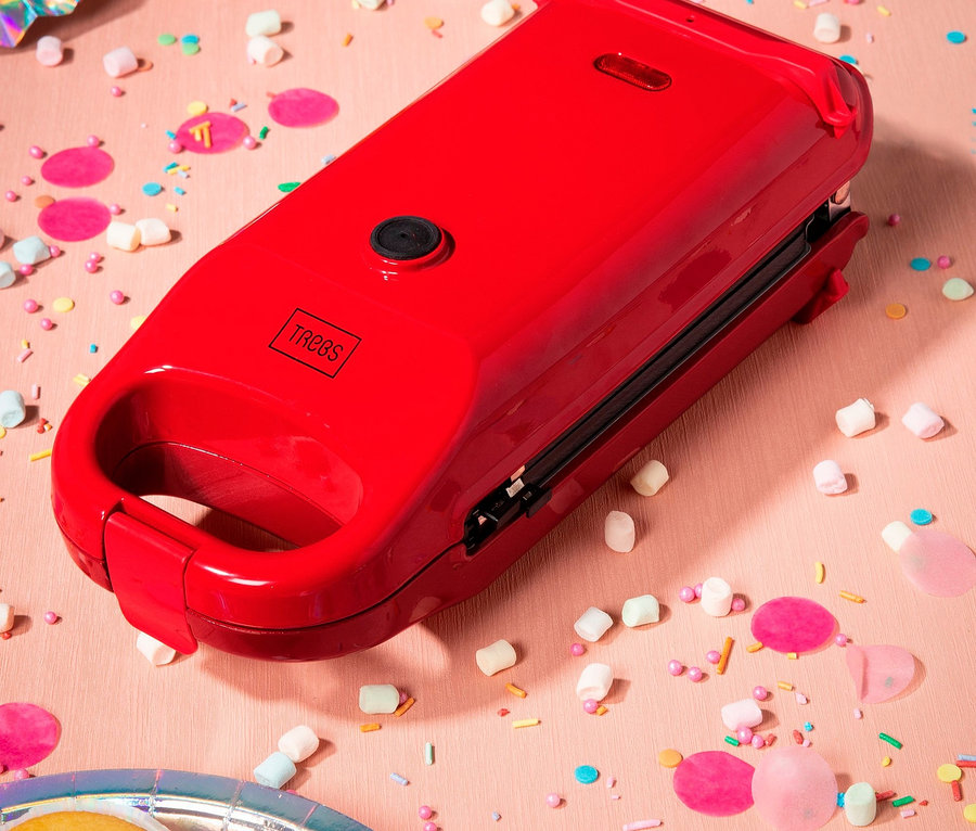 Ein roter 6-in-1-Snackmaker auf einem rosa Hintergrund mit Mini-Marshmallows und Konfetti.