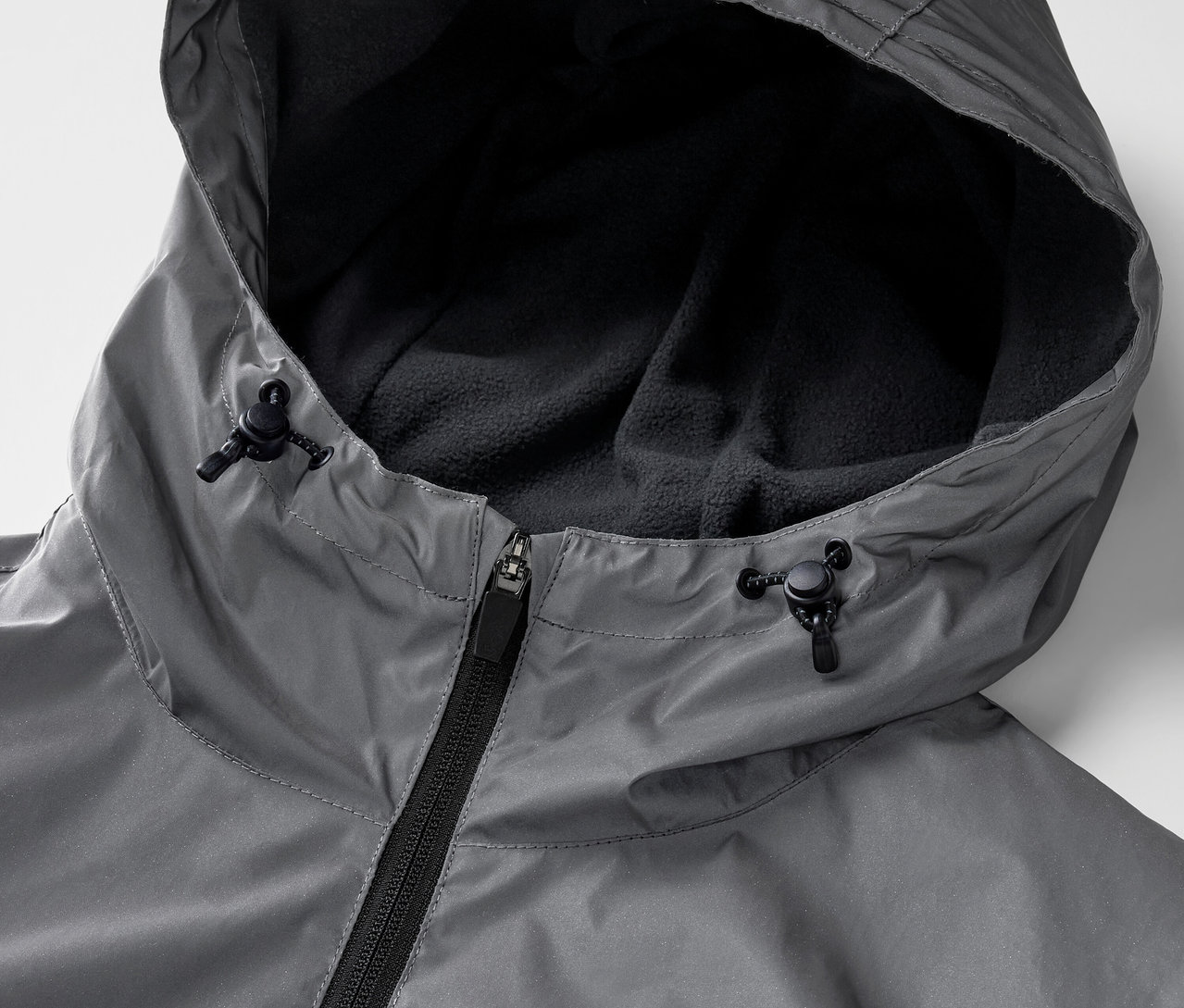 Detailaufnahme einer grauen, reflektierenden Sportjacke mit Reißverschluss und Kapuze.