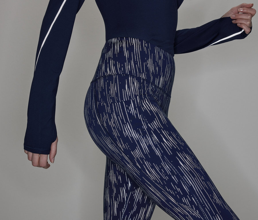 Teilansicht einer Frau in einem marineblauen Langarmshirt und gemusterten Leggings.