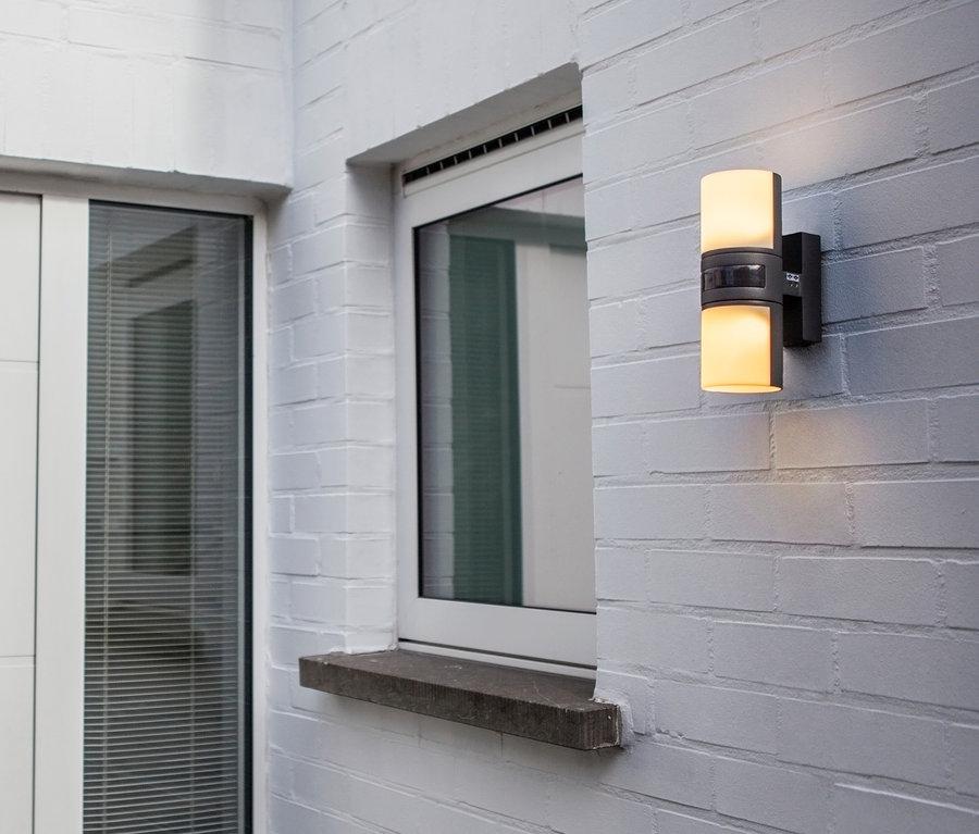 Weißes Backsteinhaus mit LED-Outdoor-Wandleuchte mit Bewegungsmelder neben Fenster und Tür.