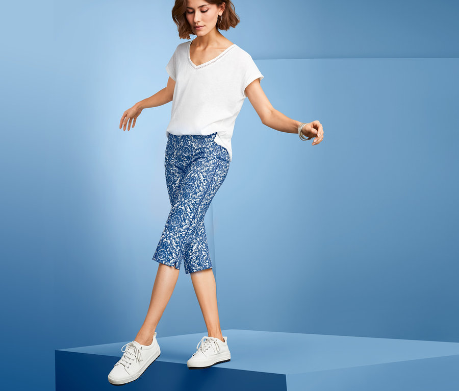 Frau geht auf blauer Plattform, trägt eine blaue, bedruckte Stretchhose in 3/4-Länge.